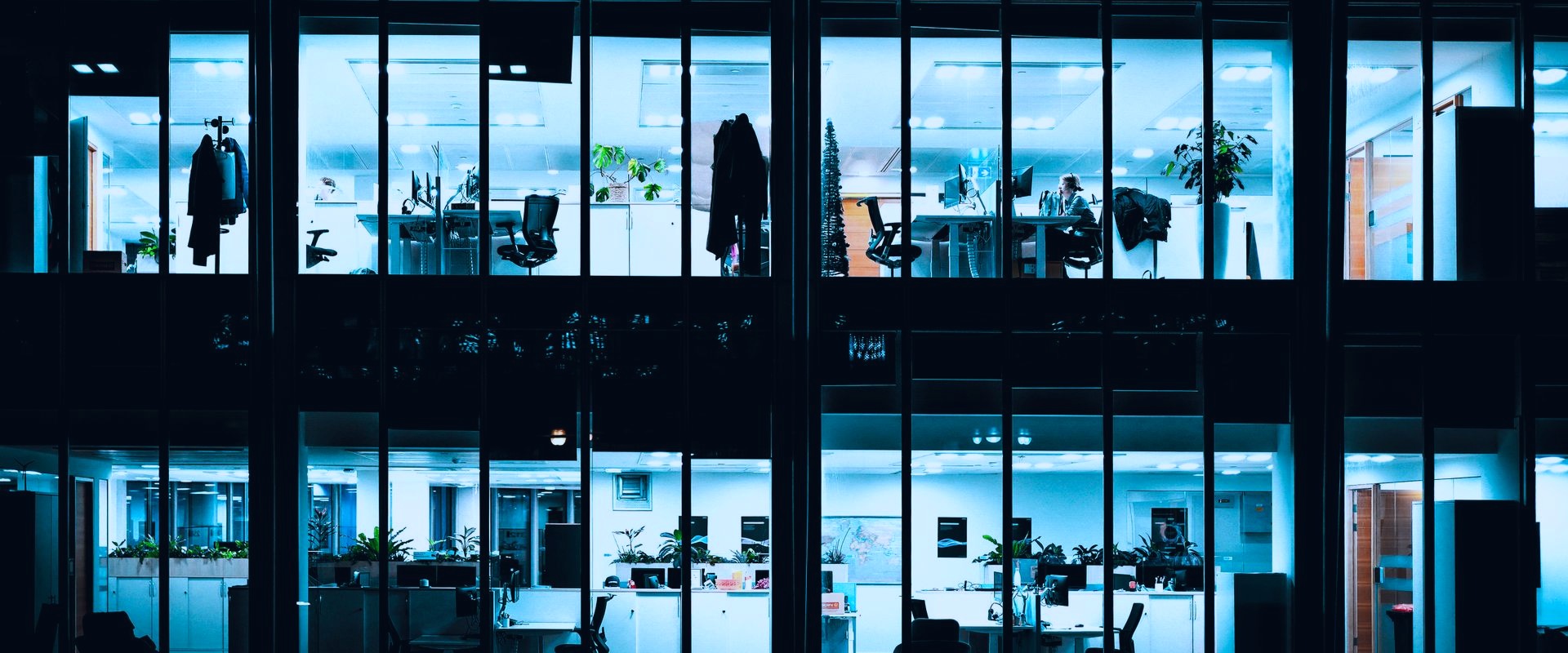 Het kantoor van Real Webdesign 's avonds, met verlichte werkplekken achter de glazen gevel